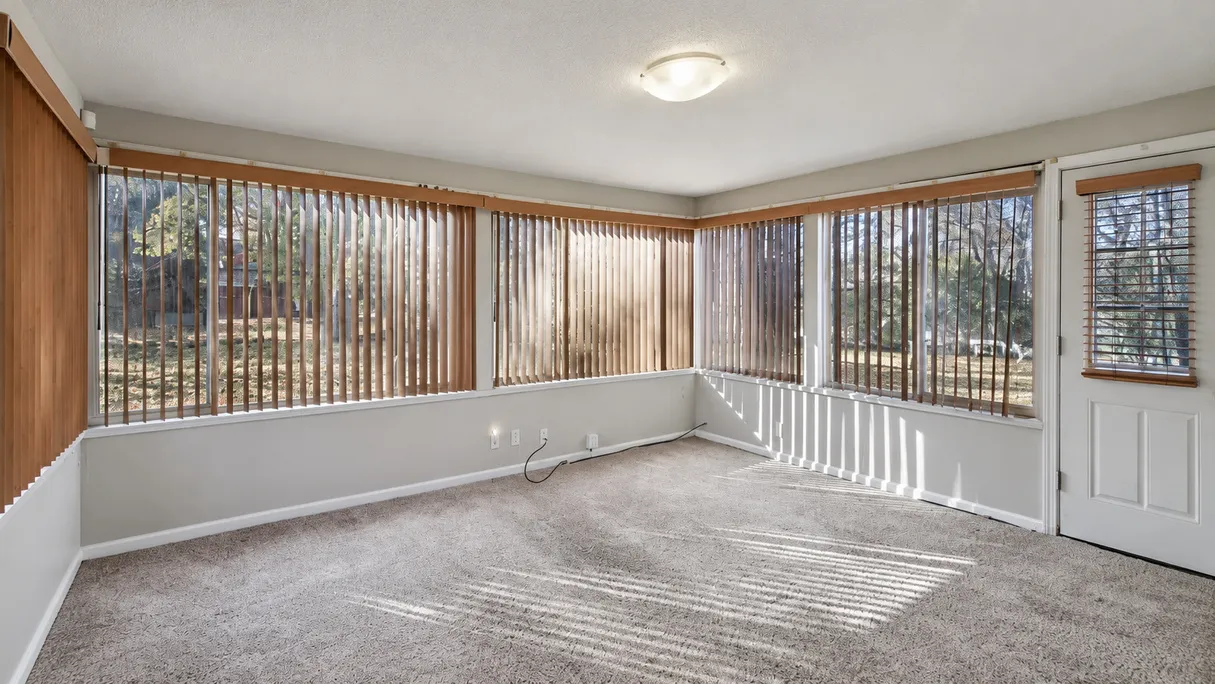 Sunroom before renovation: gray-beige carpet, vertical blinds over the windows, a flush ceiling light and gray walls